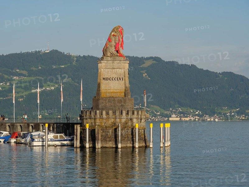 Stone sculpture of a lion at the harbour with surrounding boats and mountain view, towers at a harbour at the lake with sailing boats, Lindau, Germany, Europe