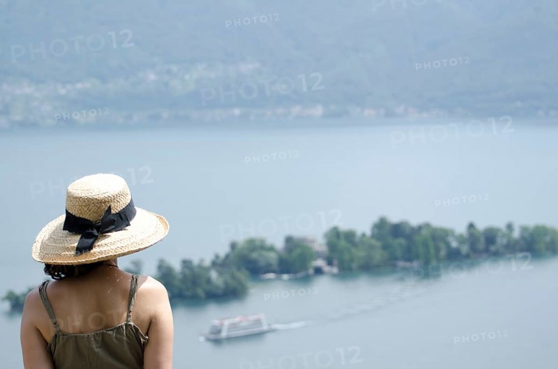 Woman with a Straw Hat Enjoy the Panoramic View over Brissago Islands and Passenger Ship on Lake Maggiore in a Sunny Summer Day in Ronco sopra Ascona, Ticino, Switzerland, Europe