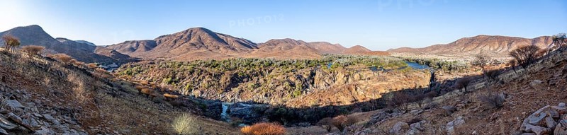 Panorama, Kunene River with green vegetation in dry red mountain landscape, waterfall and African Baobab (Adansonia digitata), in the evening light, Epupa Falls, Kunene, Namibia, Africa