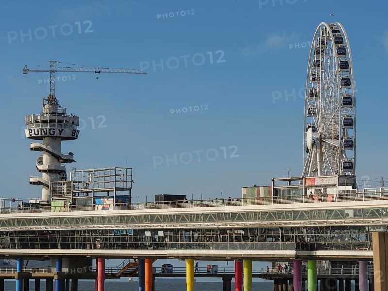 A leisure area with a large Ferris wheel and a bungee jumping tower on a colourful pier on the blue sea, sunshades and a pier on the beach of Scheveningen, Scheveningen, the Netherlands