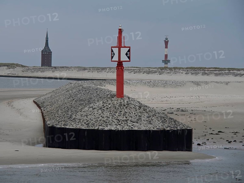 Red beacon on gravel embankment, church tower and lighthouse in the background, sand dunes and grey sky, buhne on an island in the north sea with tower and sea mark, Wangerooge, Germany, Europe