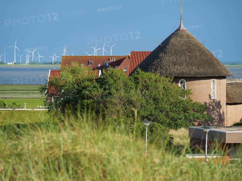 A building with a thatched roof in a lush landscape, wind turbines visible in the background, Baltrum Germany