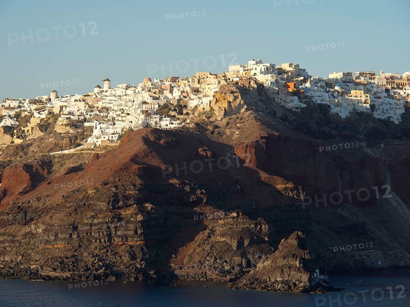 White houses on a rocky hill by the sea with a subtle evening mood in Greece, brown volcanic island in the blue sea with white houses, santorini, greece