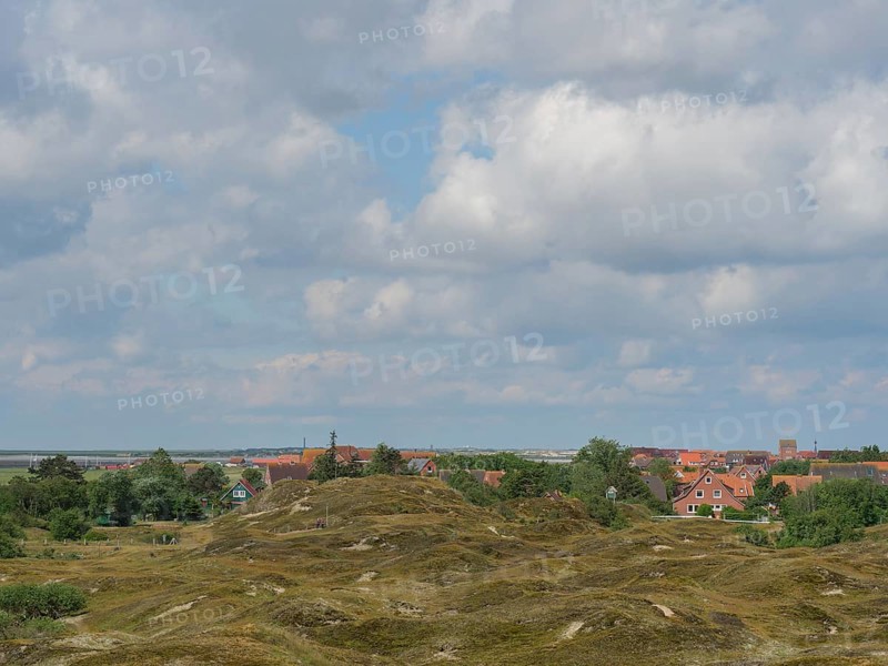 A hilly landscape with vegetation and houses in the background under a cloudy sky, Baltrum Germany