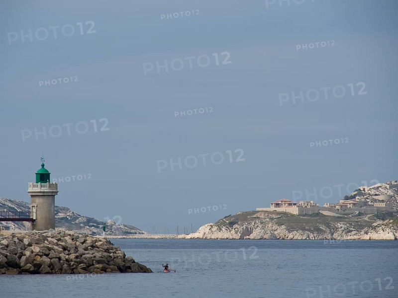 Lighthouse on a rocky coast in front of a calm sea and under a cloudy sky, Marseille on the Mediterranean Sea with the old cathedral and ships in the historic harbour, rocky coast on the mediterranean sea, marseille, france