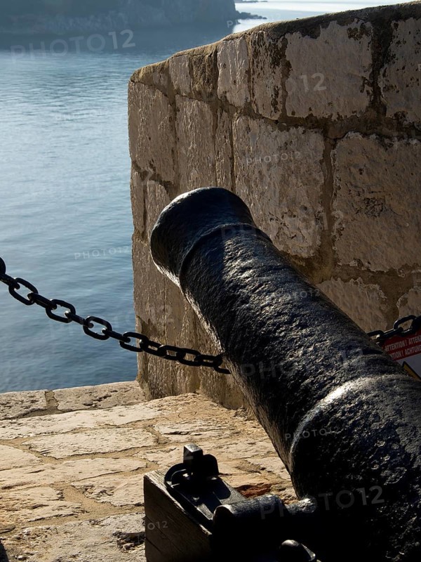 Close-up of a black cannon on an old stone wall overlooking the sea, the old town of Dubrovnik with historic houses, churches, red roofs and fortress walls, dubrovnik, coratia
