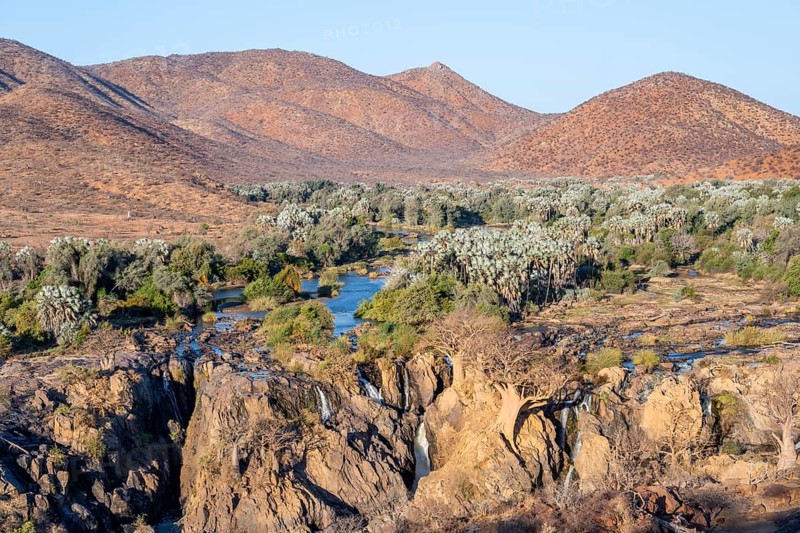 Kunene River with green vegetation in dry red mountain landscape, waterfall and African Baobab (Adansonia digitata), in the evening light, Epupa Falls, Kunene, Namibia, Africa