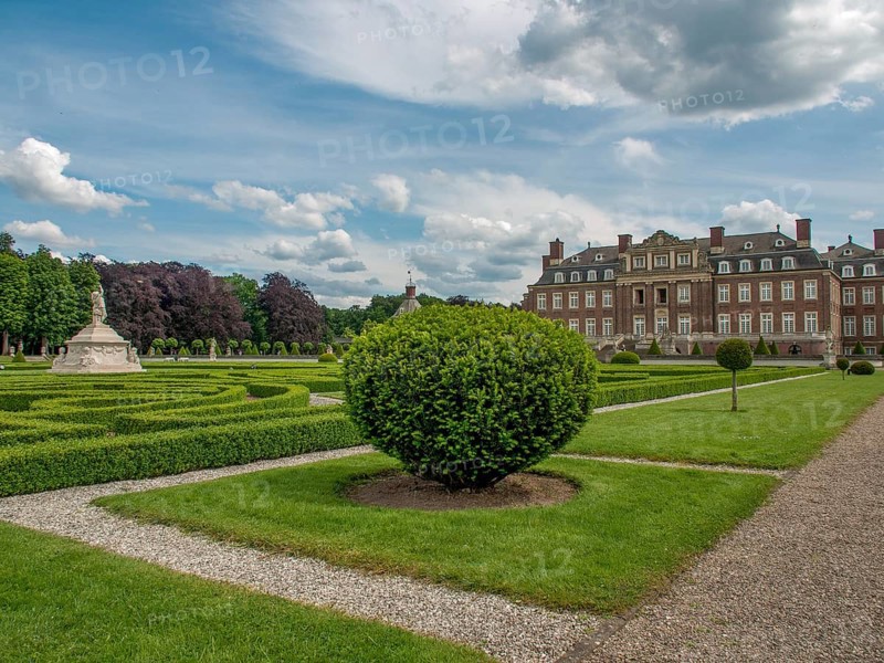 Symmetrical garden with manicured hedges and paths in front of a historic castle under a cloudy sky, historic castle with a green park with sculptures and paths, nordkirchen, germany