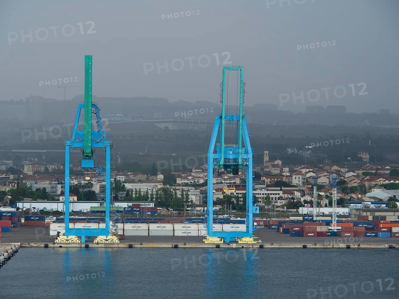 Two large blue harbour cranes in front of a cloudy industrial landscape, several containers in the harbour, Marseille on the Mediterranean Sea with the old cathedral and ships in the historic harbour, rocky coast on the Mediterranean Sea, marseille, france