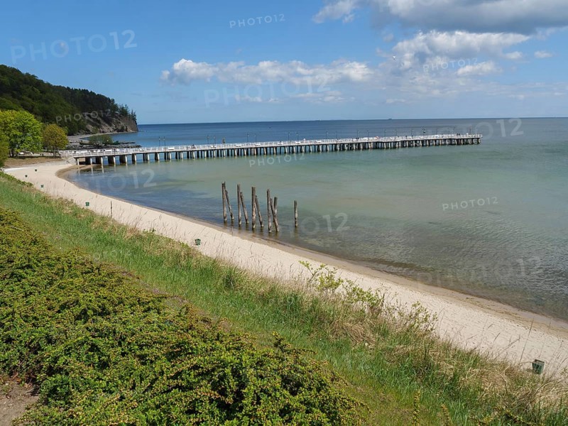 A sandy beach with a jetty leading into the sea, green coast and cloudy sky in the background, spring on the Baltic Sea coast with green fishing boats on the beach and green trees on the shore, Sopot, Poland, Europe