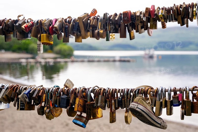 Many love locks on a railing with a lake and mountains in the background