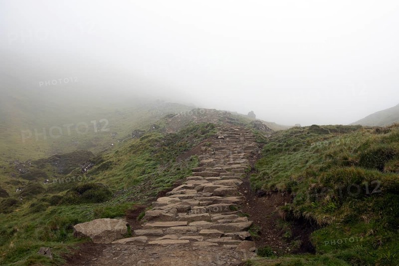 A stony footpath leads up into the misty mountains to the Old Man of Storr, the landscape is green and mystical, hidden in thick fog