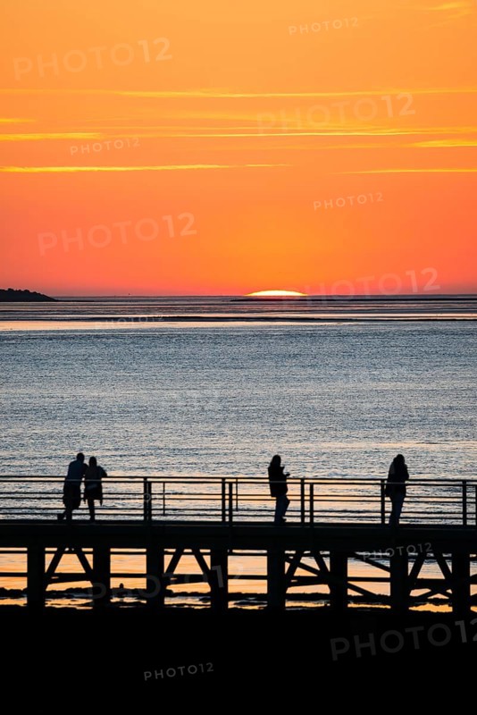 Silhouettes of several people on the pier Freilaufkanal, couple and single persons watch from a jetty the picturesque, golden, breathtakingly beautiful sunset over the sea, island Langluetjen II far away on the horizon, sun almost completely sunk, orange glowing cloudless sky, wide sea in soft colours, calm atmosphere, mouth of the Weser into the North Sea, Outer Weser, Bremerhaven, Land Bremen, Germany, Europe