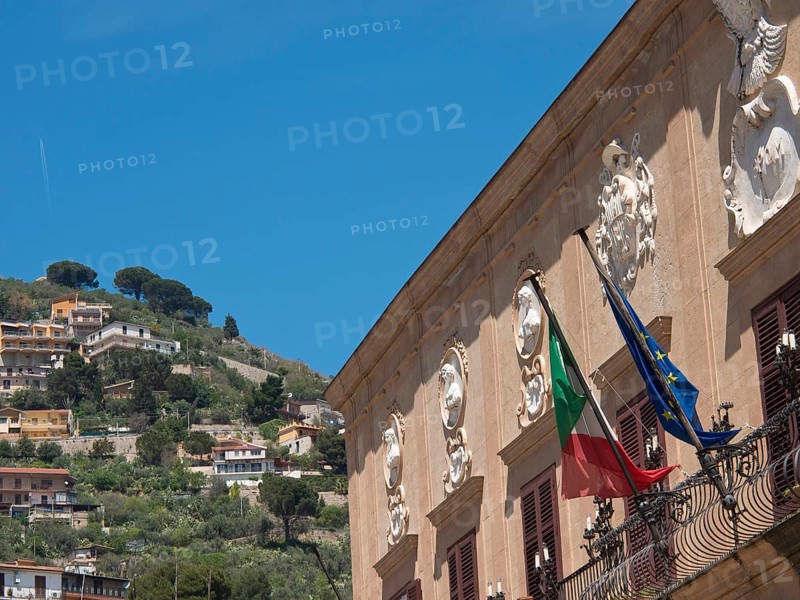 Italian and European flag building decorated and set in a hilly landscape on a sunny day, palermo in sicily with an impressive cathedral, monuments and old houses with balconies, palm trees and flowers in italy, palermo, sicily