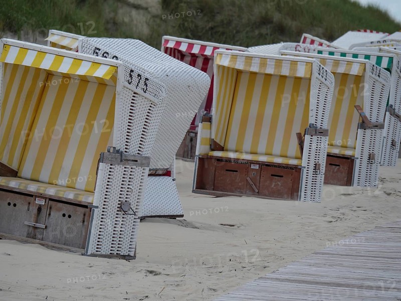 Colourful beach chairs in yellow and red on the sandy beach, the north sea island baltrum with grassy dunes, colourful beach chairs on the beach and clouds over the sea, Baltrum Germany