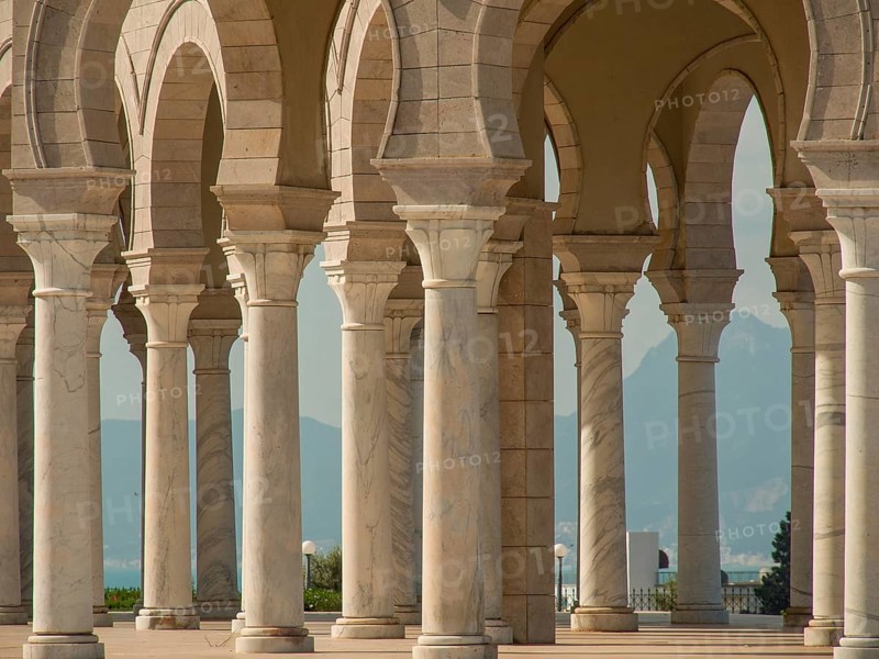 Row of marble columns with arches in brilliant daylight against a backdrop of mountains, Tunis in Africa with ruins from Roman times, modern mosques and blue and white houses in sidi-bou-said, Tunis, Tunisia, Africa