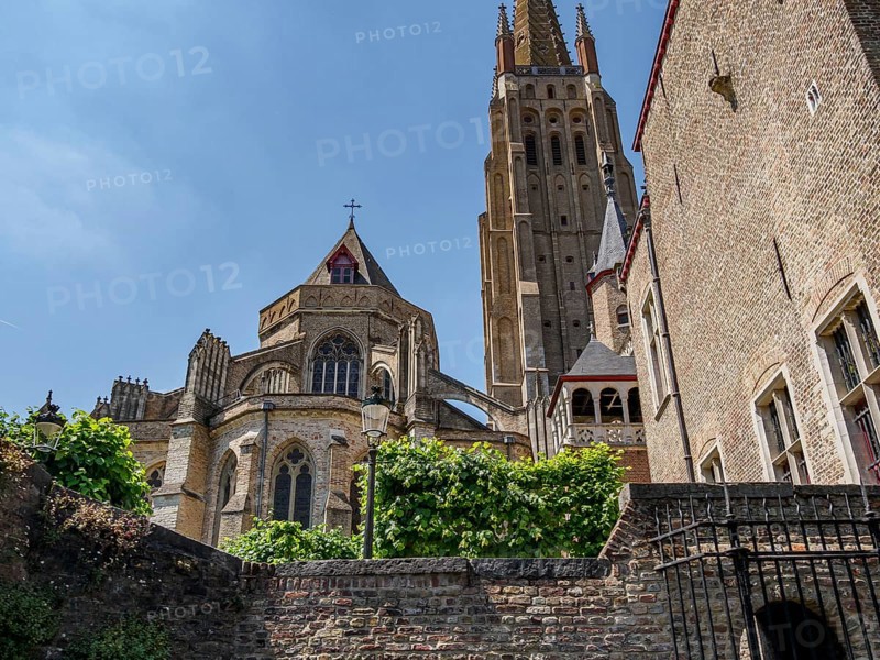 Gothic cathedral with high towers and brick walls on a summer day, historic houses and churches with towers on a river in Belgium, Bruges, Belgium, Europe