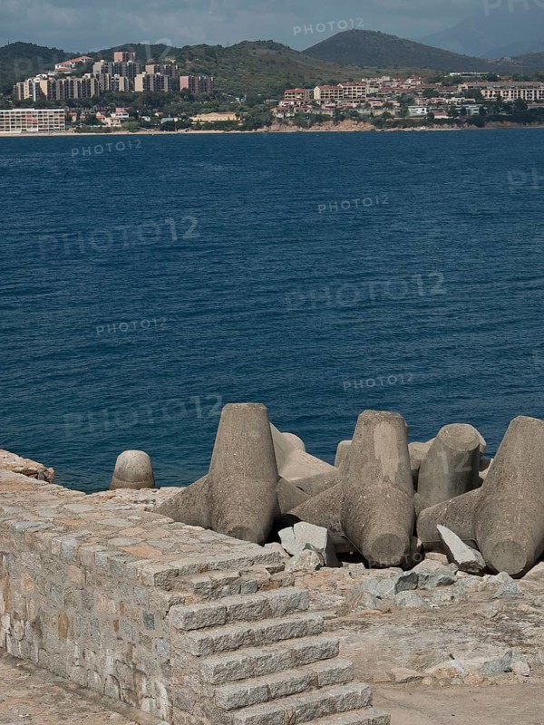 Coastline with concrete breakwaters and a view over the sea to a town and hills, Corsica, ajaccio, France, Europe