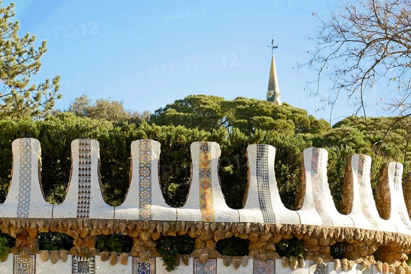 Antoni Gaudi, Park Guell, UNESCO World Heritage Site, Barcelona, Catalonia, Spain, Europe, A decorative wall with mosaic tiles and trees in the background on a sunny day, Europe