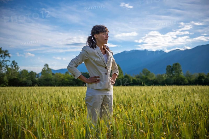Proud and elegant Woman with Her Hands on Her Hips Standing on a Wheat Field with Mountain in the Background in a Sunny Day in Locarno, Ticino, Switzerland, Europe