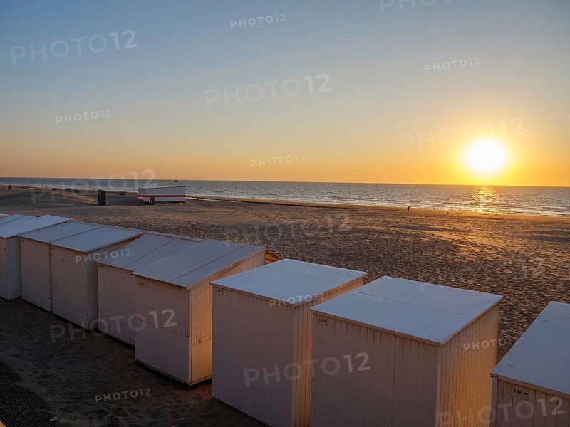 White beach huts on the beach with a view of the sunset and the sea, sunset in many colours on the beach with a calm sea, de haan, belgium