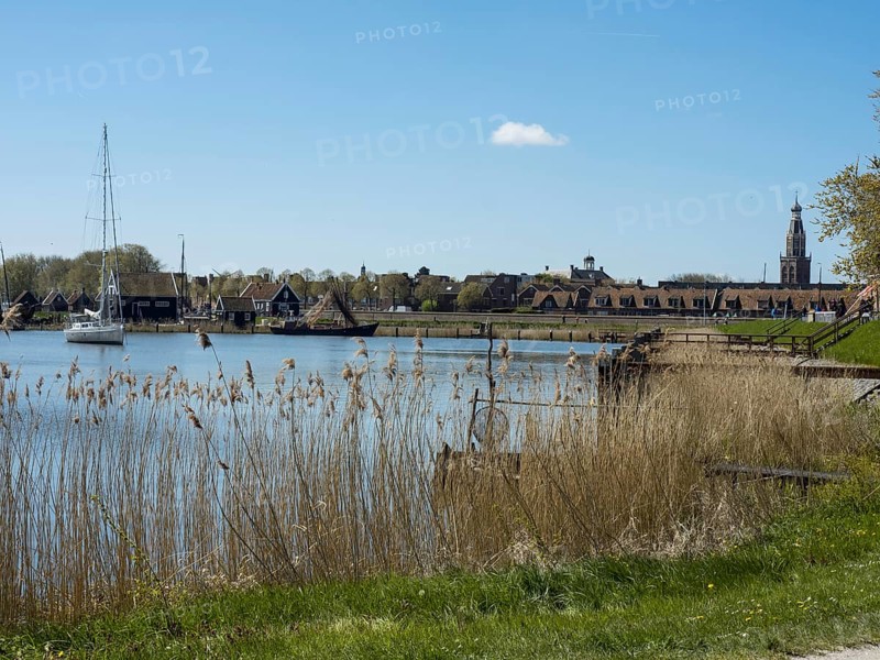 A lake with boats on the shore, a small town and a tower, reeds growing by the water, the scene appears peaceful, Enkhuizen, Nirderlande
