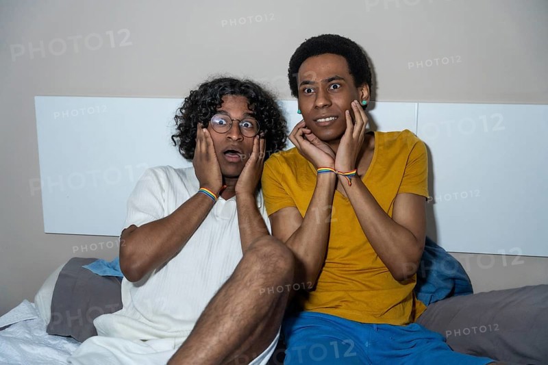 Gay latin male couple watching a horror movie at night at home