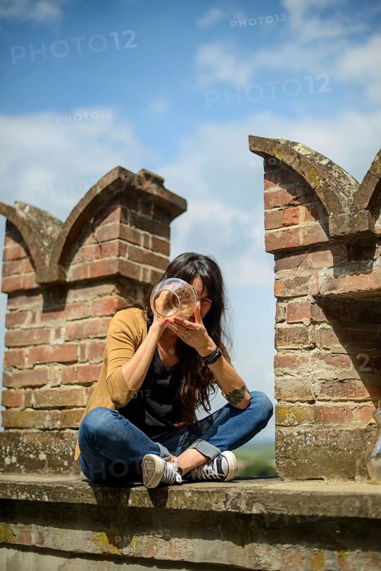 Thoughtful young woman sits on an old brick wall, casually dressed, enjoying a peaceful moment in a rustic outdoor setting