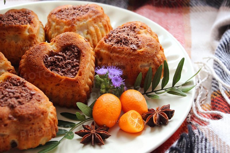Heart-shaped cakes adorned with kumquats, star anise, and a purple flower on a plate with a tablecloth