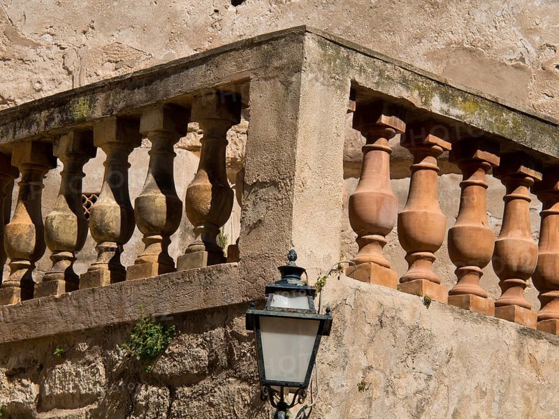 A stone balustrade on an old wall with a lamp, palma de mallorca on the mediterranean sea with its historic houses, the great cathedral and flowers, palma, spain