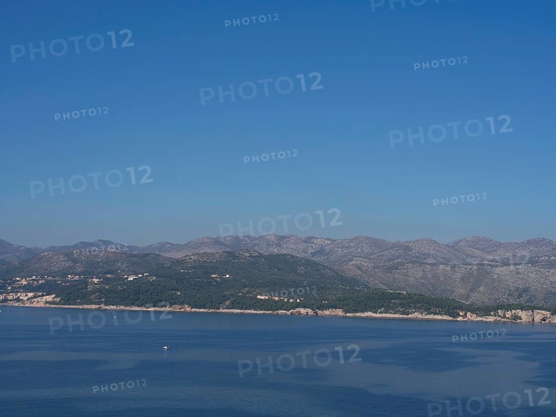 Tranquil coastal landscape with gentle mountains and clear blue skies reflected in the calm sea, the old town of Dubrovnik with historic houses, churches, red roofs and fortress walls, dubrovnik, coratia
