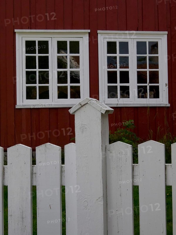 Red wooden house with two large white windows behind a willow fence, colourful wooden houses behind white wooden fences, Molde, Norway, Europe