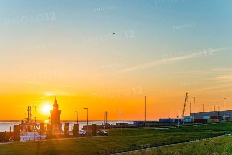 Pingelturm, historic lighthouse at the harbour at sunset, with calm sea, boats and green meadow in the foreground, sea in the background, the sky in bright orange, harbour facilities with ships, cutters, twilight, evening, dusk, maritime, calm atmosphere, mouth of the Weser into the North Sea, Outer Weser, coast, Bremerhaven, Land Bremen, Germany, Europe