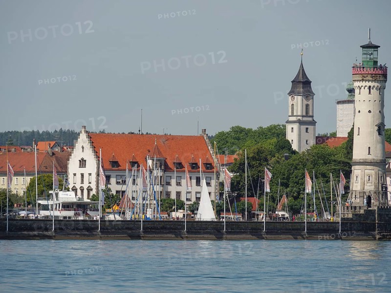 Town view with historical buildings, lighthouse and sailing boats on the calm water, towers at a harbour at the lake with sailing boats, Lindau, Germany, Europe