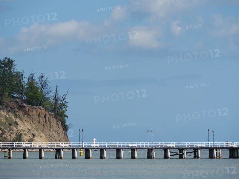 A pier next to a cliff with trees stretching into the sea under a cloudy sky, spring on the Baltic Sea beach in Poland with green trees, sopot, poland
