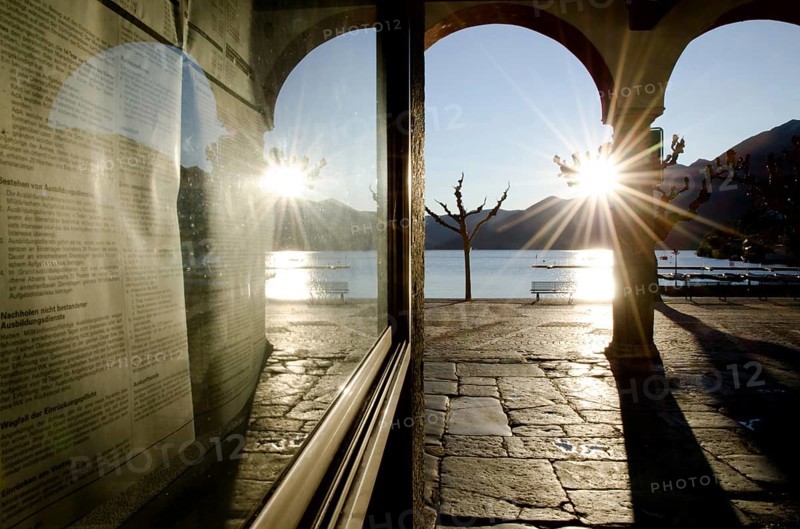 Alley with Arches on the Waterfront to Lake Maggiore with Mountain and Sunbeam and Reflection on a Window in City of Ascona, Ticino, Switzerland, Europe