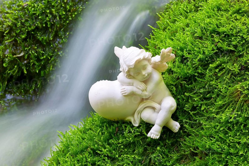 Porcelain angel figurine on moss by a waterfall
