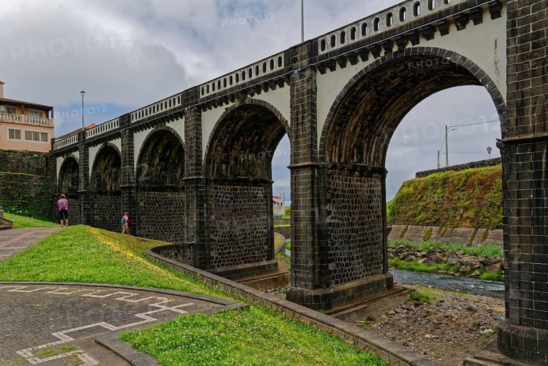 Historic eight-arched bridge over the Ribeira Grande River, surrounded by grasslands, under a cloudy sky, coastal town of Ribeira Grande, Santa Barbara, Sao Miguel, Azores, Portugal, Europe