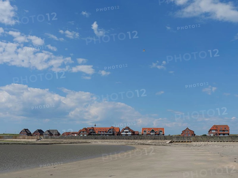 A sandy beach in front of a settlement with red houses, under a blue sky with white clouds, Baltrum Germany