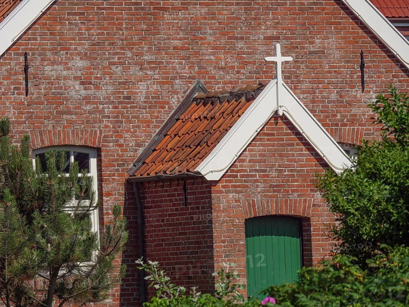 View of a brick church building with green painted door and white cross above, Baltrum Germany