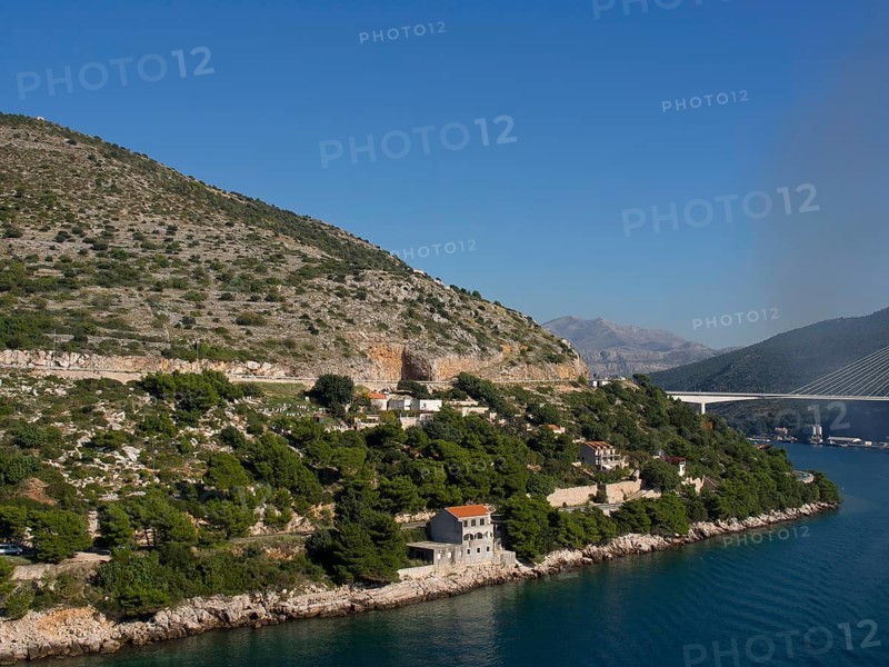 Coastal landscape with mountains, hills, bridges and houses on the shore of the calm blue sea under a clear sky, the old town of Dubrovnik with historic houses, churches, red roofs and fortress walls, dubrovnik, coratia