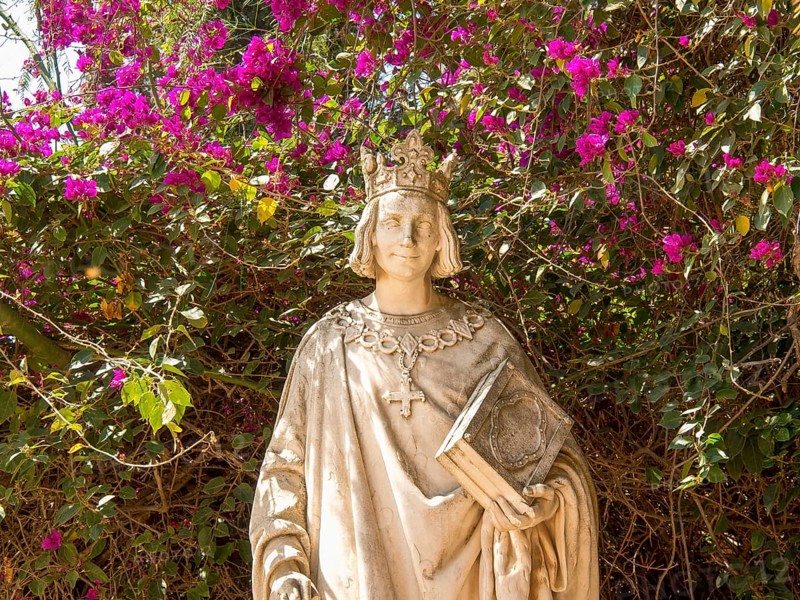 Stone statue of a king with book and cross surrounded by blooming pink flowers, Tunis in Africa with ruins from Roman times, modern mosques and blue and white houses in sidi-bou-said, Tunis, Tunisia, Africa