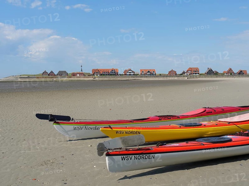 Several kayaks on the beach with a view of a coastal landscape and traditional houses, Baltrum Germany