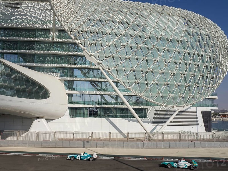 Two racing cars drive alongside a modern building with a lattice structure on the race track in competition, Abu Dhabi, United Arab Emirates, Asia