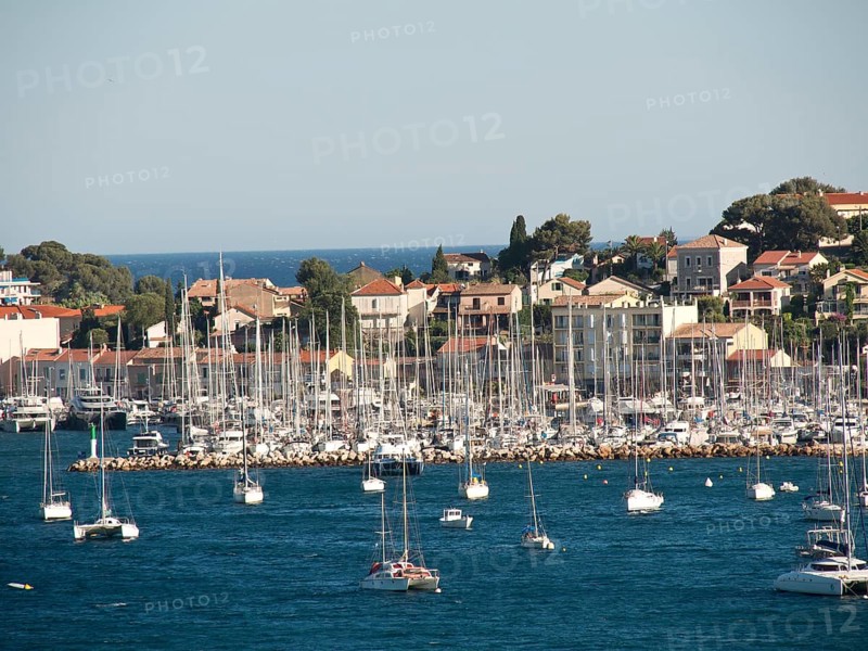 Overview of a marina with many sailing boats lying in front of a coastal town and a blue sky, la seyne sur mer on the mediterranean sea with boats in the harbour, trees and houses on the coast, la seyne sur mer, france