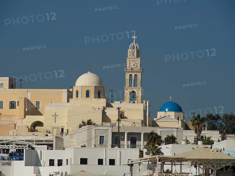View of a church with bell tower and domes against a clear blue sky, The volcanic island of Santorini with blue and white houses and churches, flowers and palm trees on a volcanic island, santorini, greece