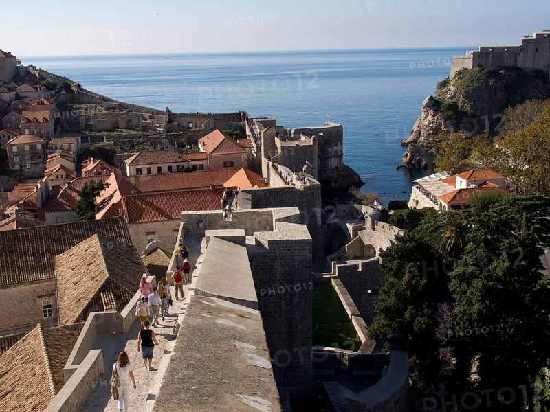People walking on a city wall with a view of the city and the sea, the old town of Dubrovnik with historic houses, churches, red roofs and fortress walls, dubrovnik, coratia