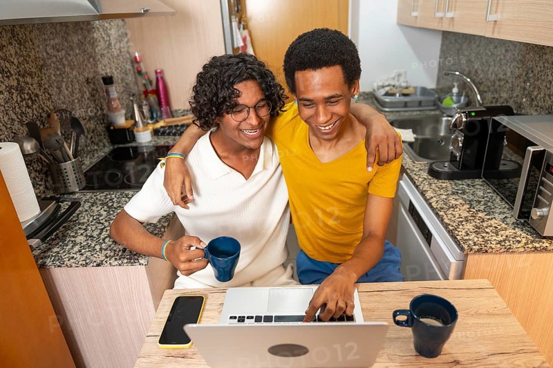 Top view photo of male gay couple using laptop sitting on the kitchen drinking coffee in the morning