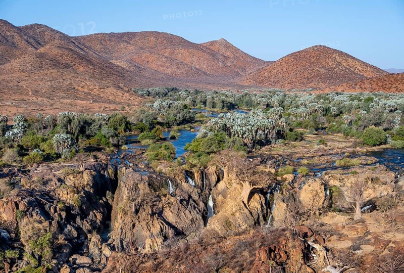 Kunene River with green vegetation in dry red mountain landscape, waterfall and African Baobab (Adansonia digitata), in the evening light, Epupa Falls, Kunene, Namibia, Africa