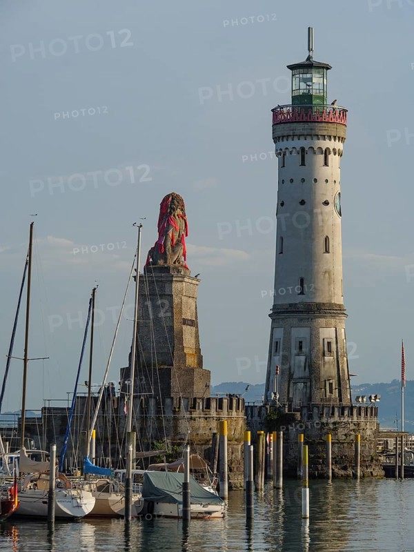 Lighthouse and lion sculpture at the harbour in late afternoon light with boats, towers at a harbour at the lake with sailing boats, Lindau, Germany, Europe